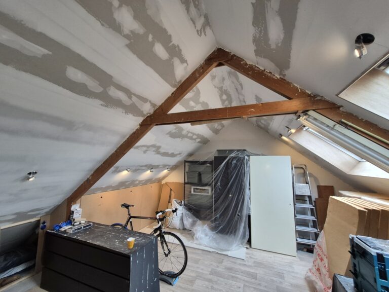 Zolder in verbouwing met geplamuurde schuine wanden en een houten spant in het zicht