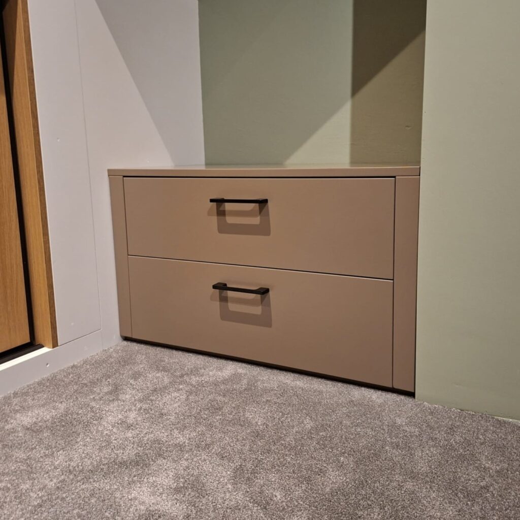 Op maat gemaakte ladekast in taupe met zwarte grepen, passend onder een schuine wand