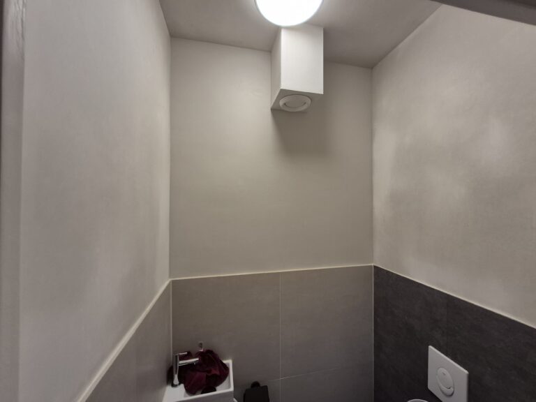 Toilet met wit gestucte bovenwand, donkergrijze tegels en een wandlamp