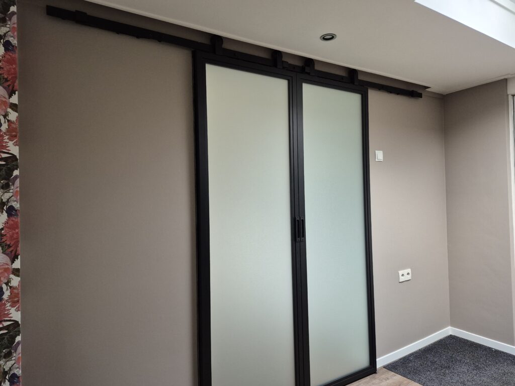 Kamer met zwarte schuifdeuren van melkglas in een warmgrijs geschilderde wand
