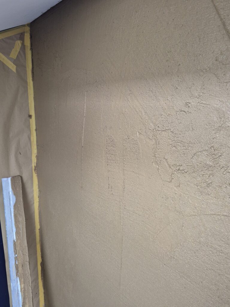 Close-up van de zandkleurige, licht gestructureerde textuur van een afgewerkte leemstucwand