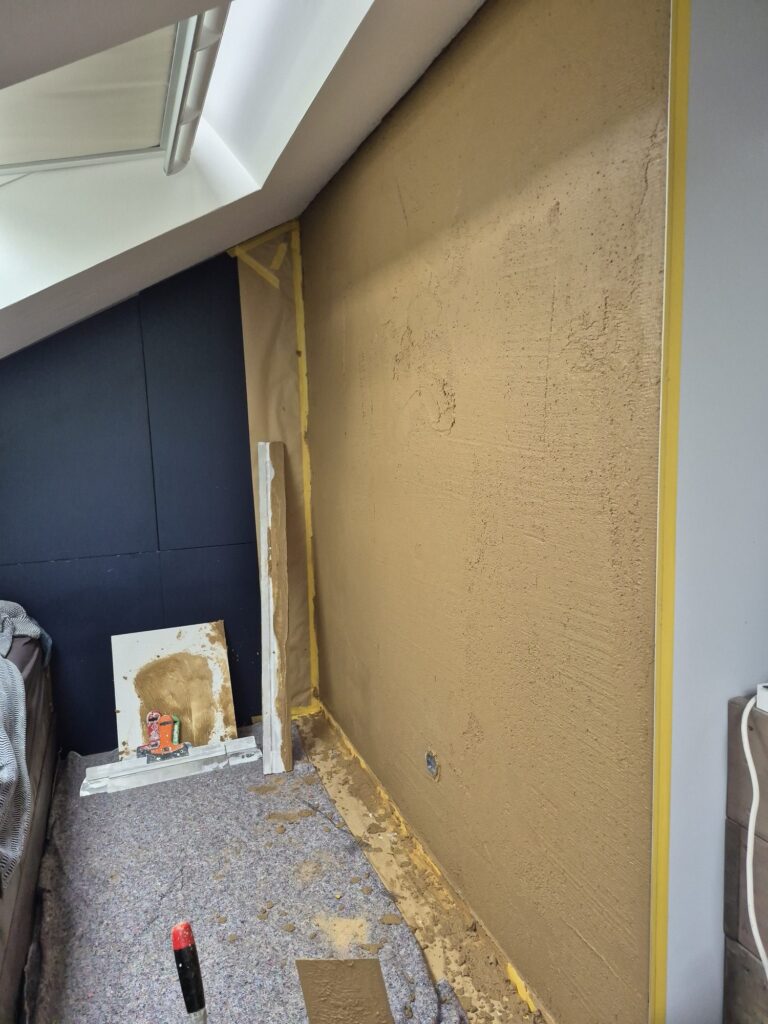 Volledig met leem gestucte slaapkamerwand in zandkleur onder een schuin dak met dakraam