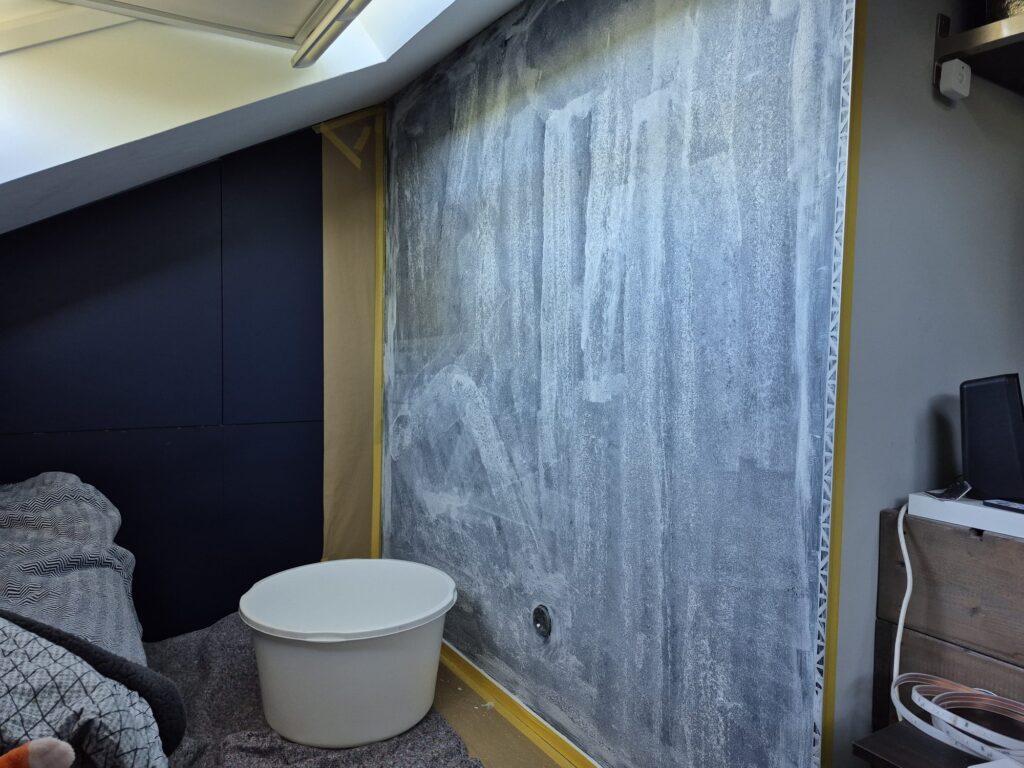Kale wand in een slaapkamer onder een schuin dak, met de randen afgeplakt met tape en afdekpapier