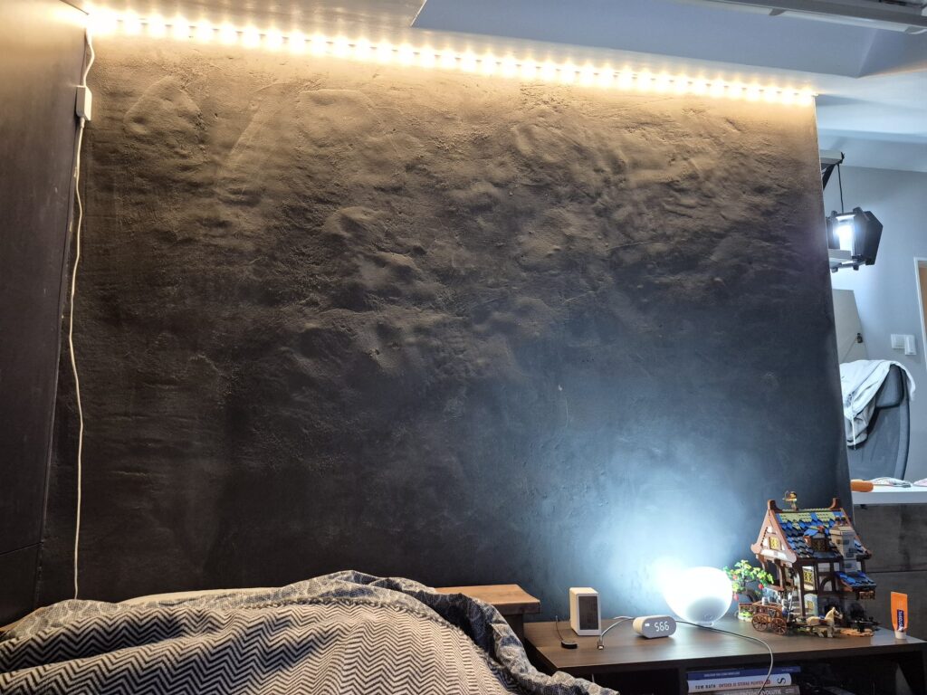 Donkere leemwand met een ledstrip langs het plafond die strijklicht geeft, waardoor bulten en deuken in het oppervlak zichtbaar worden